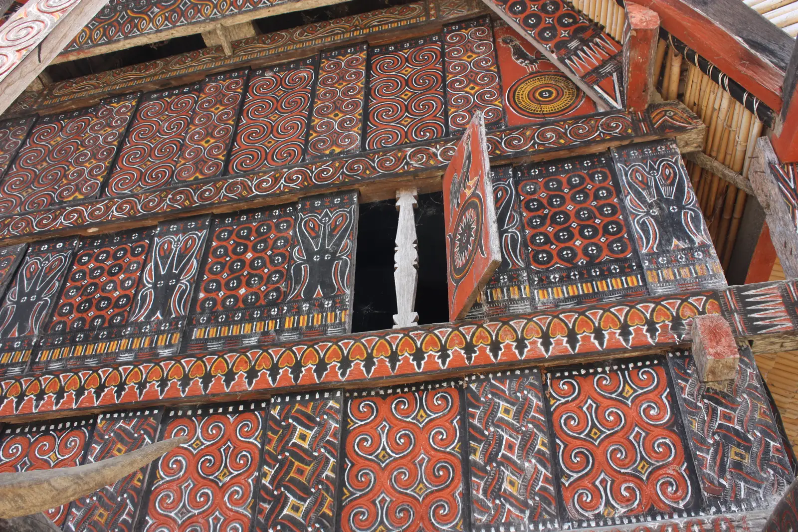 A carved and painted tongkonan gable in red, black and ochre pa’ssura patterns