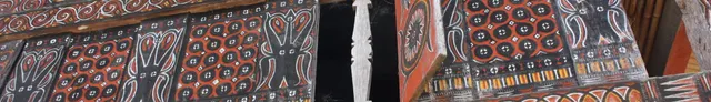 Carved detail on a tongkonan panel, a blade motif between painted roundels