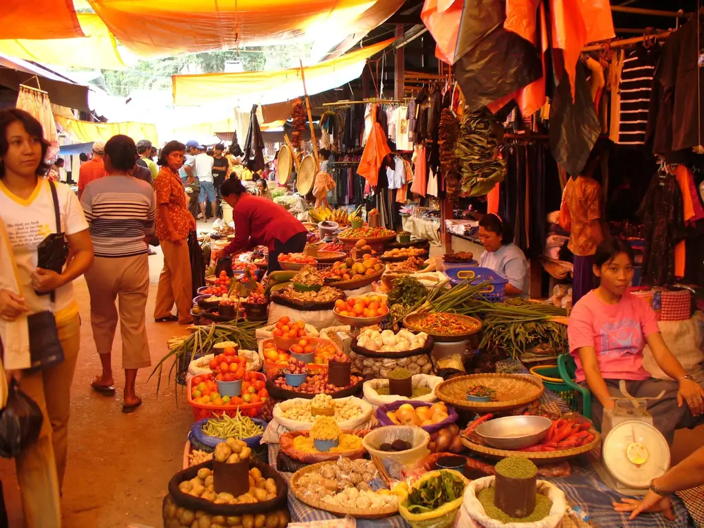 Produce stalls under awnings at the market, vendors behind baskets